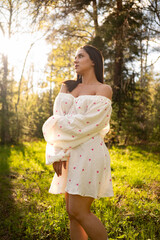 Young woman in a light summer dress standing in a sunny forest clearing