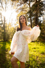 Young woman in a light summer dress standing in a sunny forest clearing