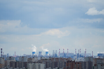 Smoking chimneys and cooling towers under dramatic cloudy sky. Concept of air pollution, urban expansion, heavy industry, and modern infrastructure in a metropolitan environment.