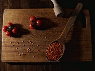 Top-down rustic food composition with red lentils in wooden spoons, cherry tomatoes, and vintage utensils on a wooden board. Warm tones, natural light, cozy organic kitchen mood.