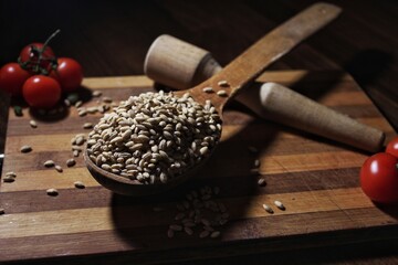 Rustic still life with raw wheat grains in wooden spoons, cherry tomatoes, and kitchen tools on a...