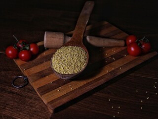 Top view rustic kitchen scene with raw millet in wooden spoons, cherry tomatoes, and utensils on a...
