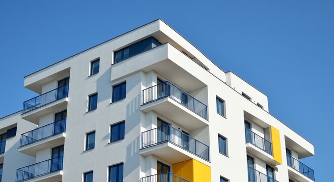 Modern White Apartment Building with Blue Balconies and Yellow Accent Against Clear Sky