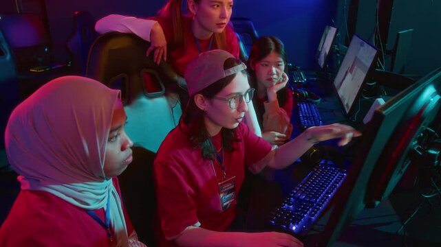 Medium shot of diverse female cyber team standing around computer screen at internet club, exploring new arena map in online video game. Perfect for online gaming marketing 