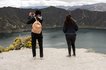Two women stand side by side on a cliff overlooking a breathtaking landscape. Their quiet...
