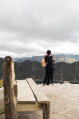 A solitary wooden chair sits near the cliff’s edge while a woman stands in the background, evoking a cinematic and suspenseful atmosphere reminiscent of iconic storytelling moments.


