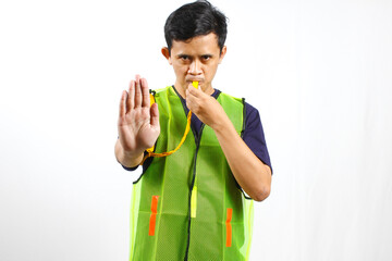 Asian parking attendant wearing green vest blowing whistle while giving stop sign