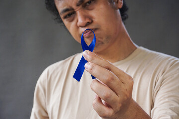 Man showing dark blue ribbon on grey background. Prostate cancer awareness, blue november, men's...