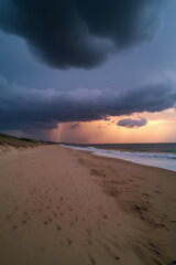 Thunderstorm approaching across a sandy beach, dark storm clouds filling the sky, distant lightning