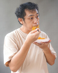 Portrait of handsome asian man eat instant noodle on grey background. He's feel surprise and...