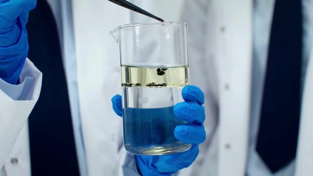 Scientist holds beaker with yellow and blue liquid layers during density experiment in laboratory