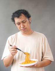 Portrait of handsome asian man eat instant noodle on grey background. He's feel surprise and...