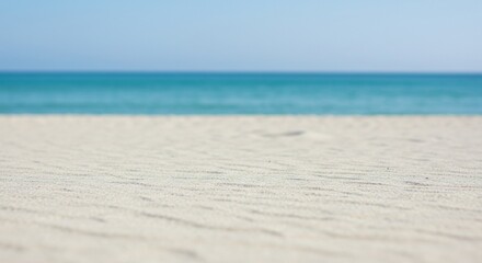 Obraz premium Soft White Sand Meets Blurred Turquoise Ocean Under Clear Blue Sky