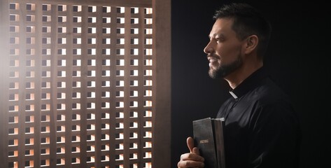 Male priest with Bible in confession booth
