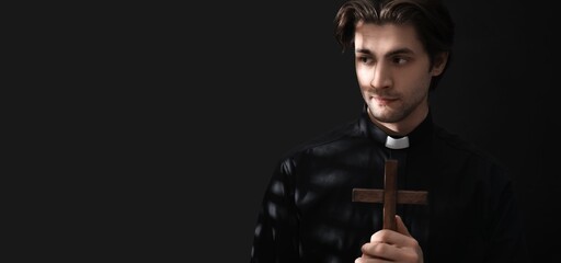 Young priest with cross on dark background with space for text