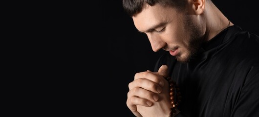 Young priest praying on black background with space for text, closeup