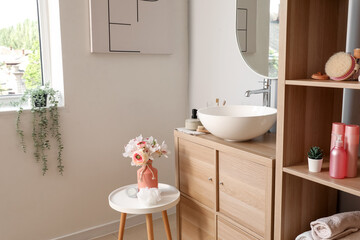 Interior of light bathroom with sink bowl, bath accessories and ranunculus flowers