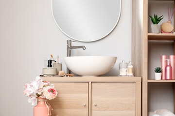 Interior of light bathroom with sink bowl, bath accessories and ranunculus flowers