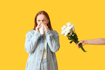 Allergic young woman and hand with flowers on yellow background