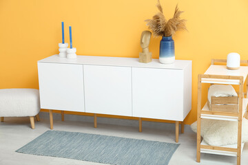 Stylish interior of living room with drawers, bench, shelving unit and soft rug