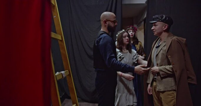 A theatre director guides young actors backstage, offering advice and encouragement as they prepare for a performance.