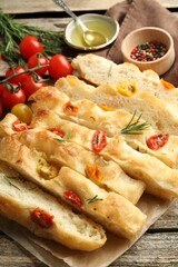 Cut delicious focaccia with tomatoes, spices and oil on wooden table, closeup