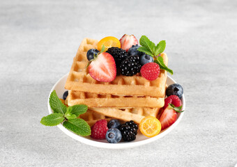 Stack of crispy Belgian waffles with raspberries, blackberries and blueberries on a gray...