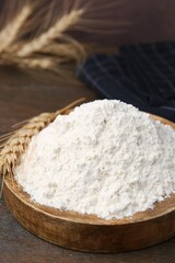 Wheat flour and spikes on wooden table, closeup