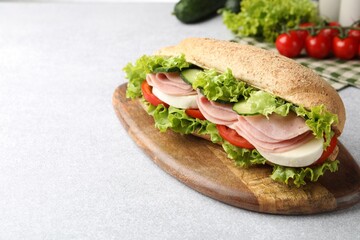 Tasty baguette sandwich with ham and vegetables on light grey table, closeup. Space for text