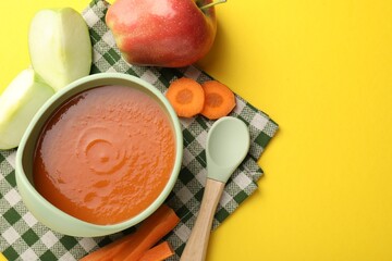 Baby food. Tasty puree in bowl and ingredients on yellow background, flat lay. Space for text