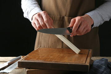 Man sharpening knife with sharpener on wooden table, closeup