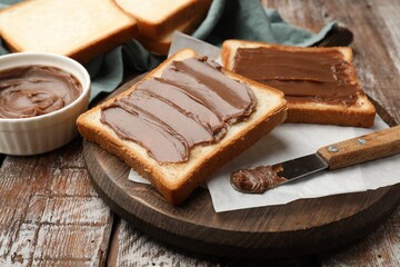 Sandwiches with chocolate butter and knife on wooden table, closeup