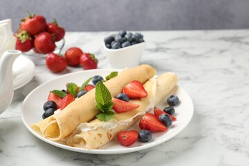 Tasty crepes with cream, berries and mint on white marble table, closeup