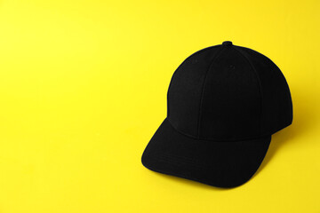 Black baseball hat on yellow background, space for text