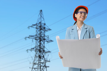 Power engineer in hard hat holding draft against high voltage tower