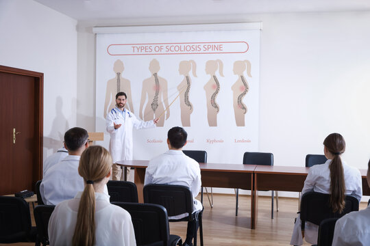 Healthcare professional giving lecture about scoliosis in conference room using video projector. Illustrations on projection screen