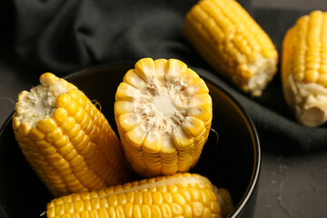Bowl with cut fresh corn cobs on black background