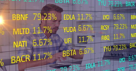 Typing mid adult man in blue checked shirt reviewing ticker overlay on laptop in modern office