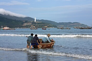 three fishermen pushing  a woven bamboo circular fishing boat out from the beach in da nang in...