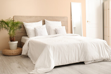 Comfortable bed with white pillows, mirror and houseplant in bedroom