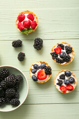 Tasty tartlets with whipped cream and berries on green wooden background