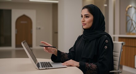Confident Emirati businesswoman uses laptop, showcasing modern Arab professionalism.
