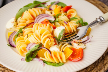 Plate of tasty pasta salad with pepper and red onion, closeup