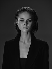 black and white woman portrait with wet hair and serious expression wearing dark blazer on dark...