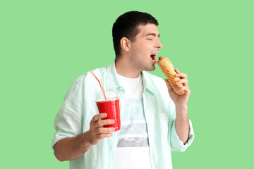 Fototapeta premium Young man with tasty french hot dog and drink on green background