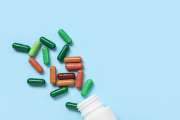 Jar with different scattered pills on blue background