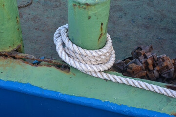 white rope on an iron pole. A thick white rope is wrapped around a green metal bollard, securing a...