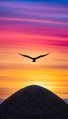 Naklejka premium Silhouette of bird flying over a blue and purple hill at sunset