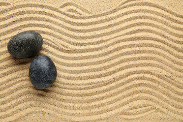 Black spa stones on sand with lines, closeup. Zen concept