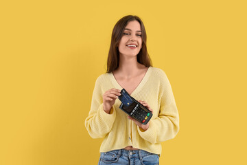Young woman paying with credit card via terminal on yellow background